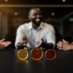 Three glasses with progressively darker liquids on a table in front of three people having a conversation.