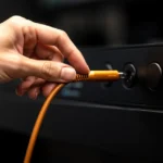 Hand plugging an orange power cord into a black electrical outlet strip.