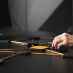 Designer arranging black and gold square tiles connected by orange lines on dark table workspace