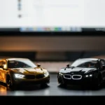 Gold and black die-cast BMW model cars on a dark surface with a computer monitor in the background.