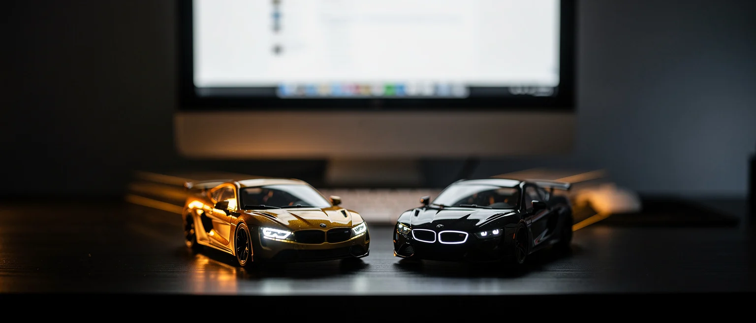 Gold and black die-cast BMW model cars on a dark surface with a computer monitor in the background.