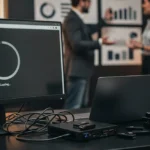 Monitor displaying a loading spinner with "Loading..." text, with colleagues and charts visible in the blurred background.