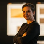 Woman in black shirt standing with crossed arms in front of illuminated panels with yellow and beige squares.