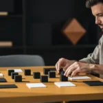 Man arranging black and white sample swatches on a wooden table indoors.