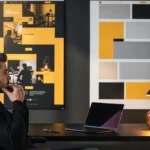 Man at desk with laptop studying design mood boards on wall behind him.