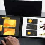 Person viewing design presentations on two tablets displaying yellow and orange UI mockups and charts.