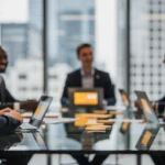Business professionals in formal attire seated around a conference table with laptops, overlooking a city skyline.