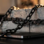 Heavy black chain draped across concrete blocks on a dark surface in warm lighting.